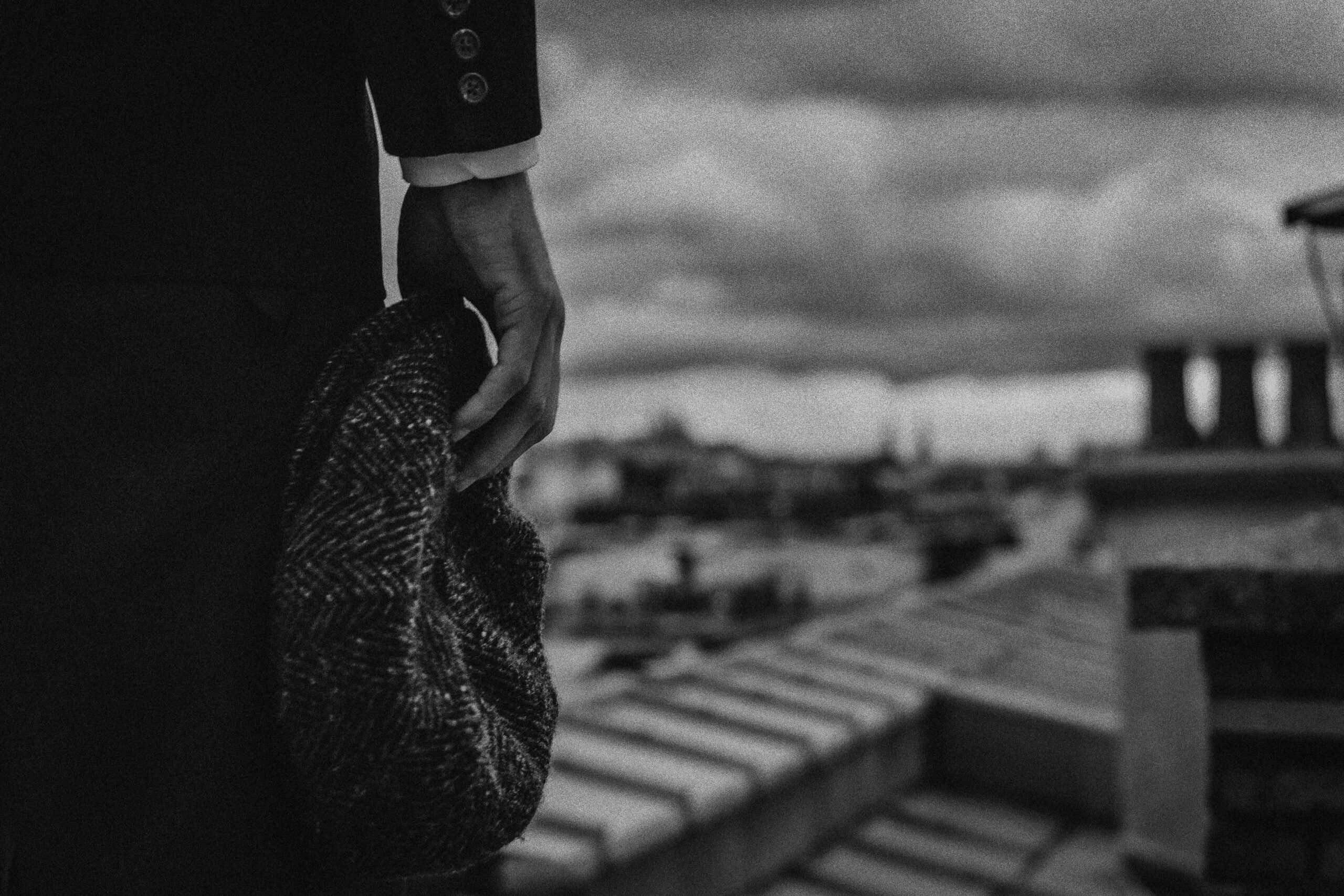 A moody black and white photo of a person holding a beret on a Paris rooftop.