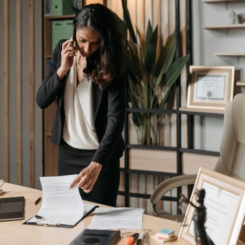 A female lawyer talking on phone while reviewing legal documents in a modern office setting.
